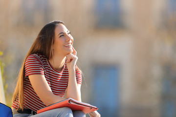 Happy student thinking looking at side in a campus
