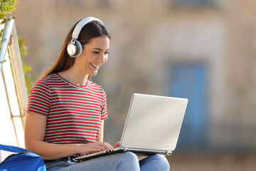 Happy student e learning with headphones and laptop in a campus