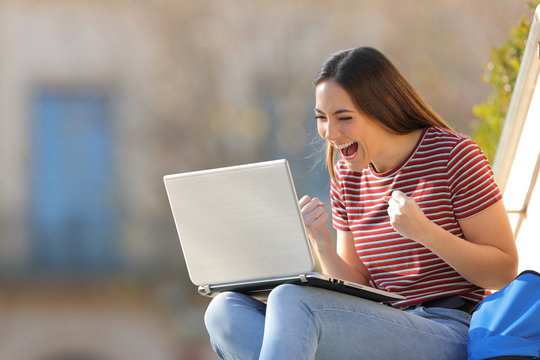 Excited student checking good news on laptop in a campus