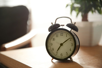 Naklejka premium Alarm clock on wooden table at home. Morning time