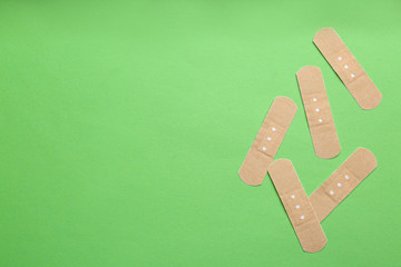 Sticking plasters on green background, flat lay. Space for text