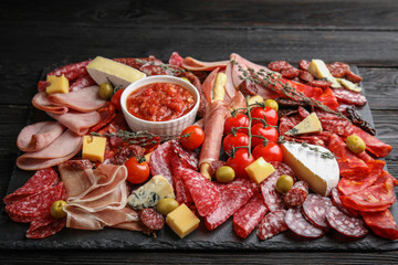 Tasty ham with other delicacies served on black wooden table