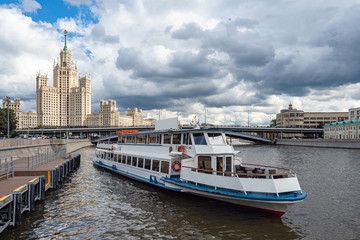 Fototapeta na wymiar Pleasure boat sails from the pier. The beginning of the water tour of Moscow. Tourist attractions of Moscow. High-rise building in the center of the capital. Travel to Russia. Cloudy day.