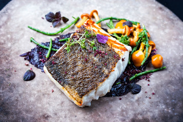 Gourmet fried European skrei cod fish filet with glasswort, fungi and algae as closeup on a modern design plate