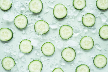 Pattern with freshly cut cucumber slices and ice cubes on green background