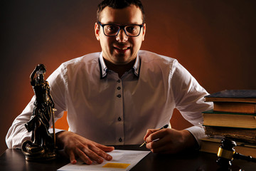 Smiling male lawyer on his desk with paperwork. Libra and wooden gavel and books