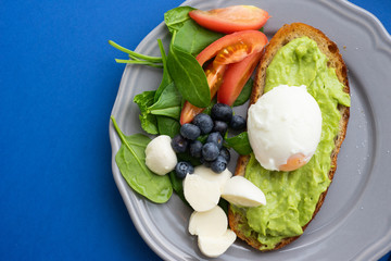 Wholesome tasty full of vitamins and health breakfast with avocado, berries, cheese and tomatoes with basil on classic blue background. Detox. Healthy food. Soft focus and beautiful bokeh.