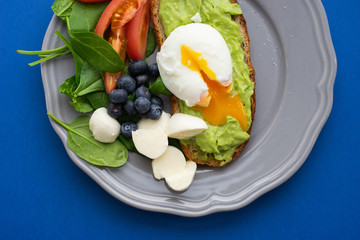 Wholesome tasty full of vitamins and health breakfast with avocado, berries, cheese and tomatoes with basil on classic blue background. Detox. Healthy food. Soft focus and beautiful bokeh.