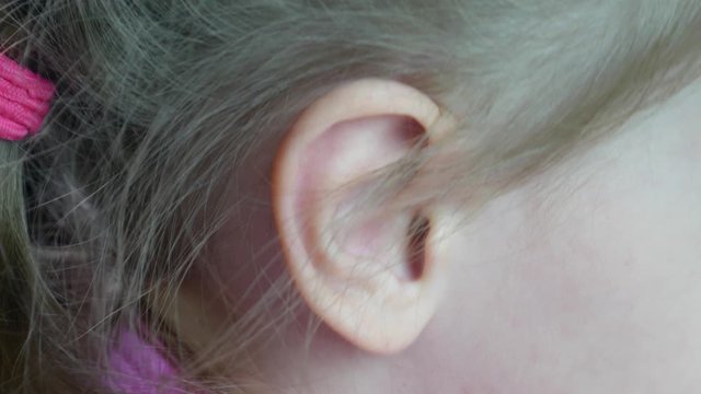 Little girl wiggles her ear in close-up. Blonde girl's ear