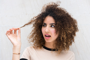 Close up young woman pulling curly hair looking with puzzled expression