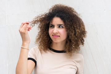 Close up young african american woman holding curly hair with unhappy expression on face
