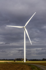 Obraz premium Éolienne entière durant un coucher de soleil avec beaucoup de nuages dans un champs - Parc éolien à fort impact visuel