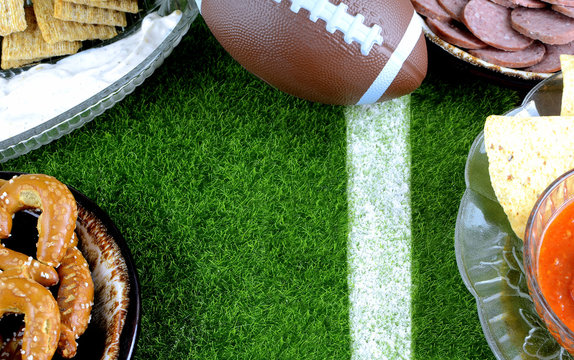 Snacks for watching a football game. Great for Super Bowl or Playoff themed projects. Pretzels, sausage, chips and dips with a football and a faux grass background