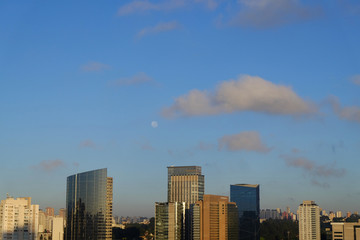 Fototapeta na wymiar Flat cityscape with blue sky, white clouds and moon. Modern city skyline flat panoramic background. Urban city tower skyline illustration