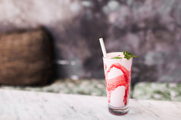 Fresh tasty cold milk shake with red strawberry syrup on white marble table. Gray concrete background. Sweet frappuccino beverage. Summer drink concept.