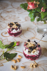 Top view on a bowl of organic cottage cheese yogurt with black currants, granola and cashew on a table with a vase and a bouquet of garden roses in the background. Healthy eating concept. Toning