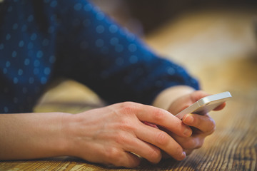 A young girl with a phone in her hands sits at a wooden table and types text using the touch screen of the phone. Modern communication technologies. Toning and artificial noise