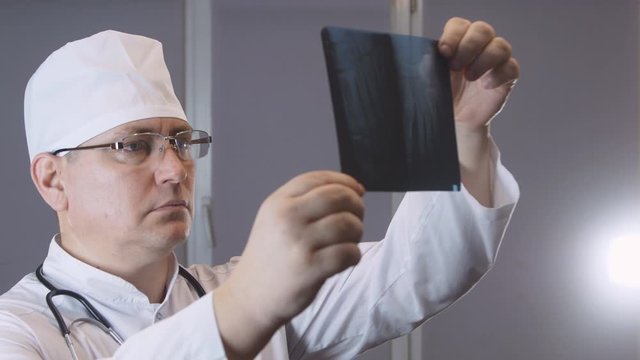 Doctor man in glasses, in a white coat, with a phonendoscope examines a picture of an x-ray of the toes, the concept of medicine