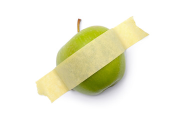 A green apple glued with yellow tape to a white surface. Modern pop-art.