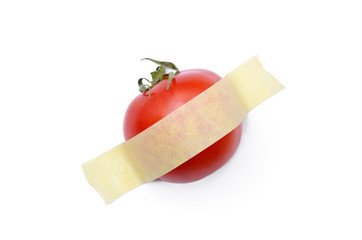 Tomato glued with yellow tape to a white surface. Modern pop-art.