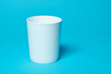 White ceramic cup isolated on a blue background. Free space for text. Simplicity