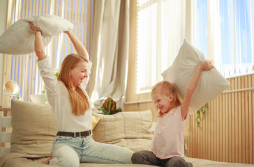 Mother and daughter joyfully play together with pillows at home in bedroom