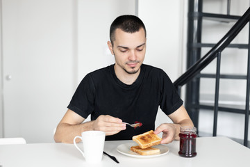 The guy has breakfast with toast with jam.