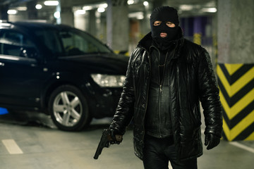 Terrorist or gangster in black jacket, gloves and balaclava holding handgun