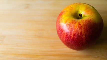 Naklejka na ściany i meble An apple on bamboo wood chopping board, red apple with yellow spots