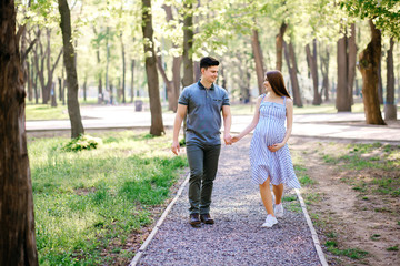 Obraz premium Young expectant mother and her boyfriend are walking in the park, husband and wife are walking in the fresh air waiting for the child