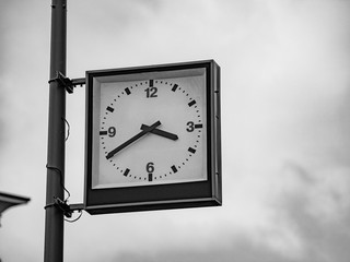 Street clock with a traditional dial and hands arrows for hours and minutes. An rectangular boxed...