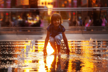 Child play with street fountain touching water on Philadelphia square over sunset near city hall in...