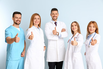 Fototapeta na wymiar Team of doctors showing thumb-up gesture on color background