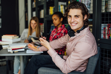 Young man with black hair reading a book, teenager in casual clothes in library.