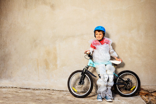 Boy with bicycle ball wear overprotecting super safe bubble wrap cover and helmet stand near the grey wall on the street