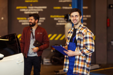portrait of smiling repairman in uniformn with clipboard looking at the camera with a client standing on the background