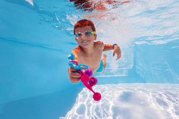 Cute happy boy swim underwater in the pool diving collecting colorful toys wearing googles