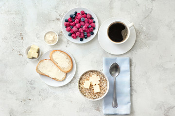 Tasty breakfast with oatmeal, fresh bread, butter, berries and cup of coffee on white background