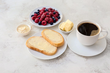 Tasty breakfast with fresh bread, butter, berries and cup of coffee on white background