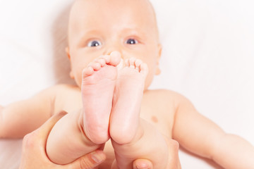 Close-up of baby feet hold by mother with infant face and look on background