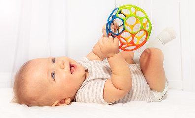 Fototapeta Little cute baby boy toddler play and hold toy ball laying on the back laughing obraz