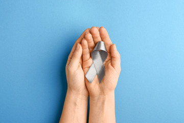 Female hands with silver ribbon on color background