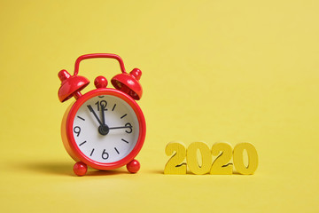 Wooden figures 2020 on a yellow background with red clocks.
