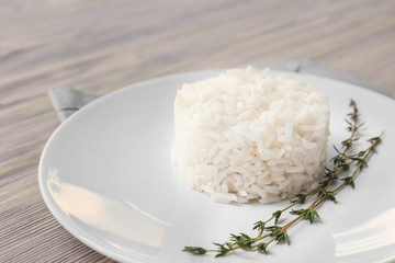 Plate with boiled rice on white wooden background