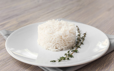 Plate with boiled rice on white wooden background