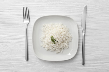 Plate with boiled rice on white wooden background