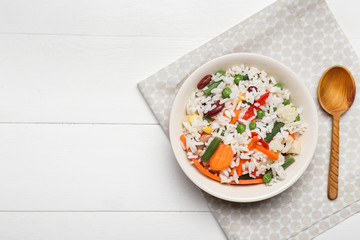 Bowl with boiled rice and vegetables on white wooden background