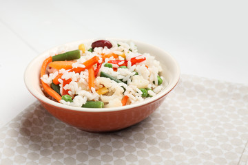 Bowl with boiled rice and vegetables on white background