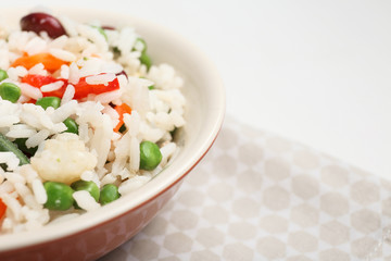 Bowl with boiled rice and vegetables on white background, closeup