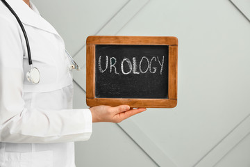 Doctor holding chalkboard with text UROLOGY on grey background